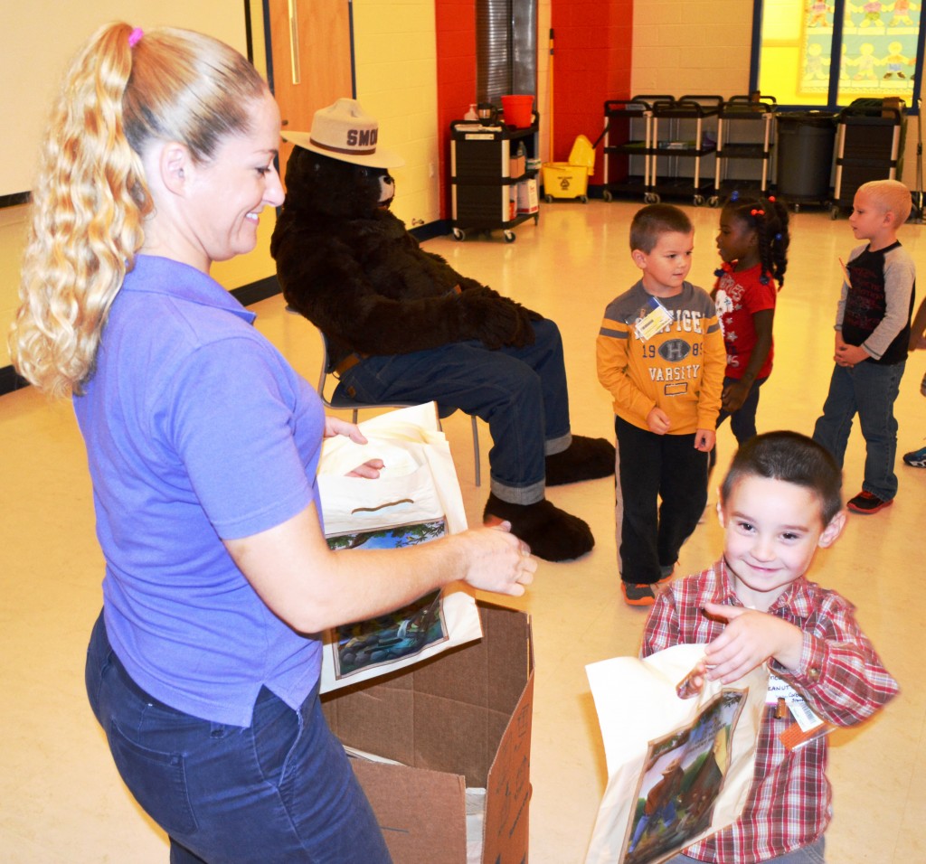 Delaware Forest Service Education Coordinator Ashley Peebles hands a gift bag of Smokey Bear school supplies to James Callis, one of 535 kindergarten students at McIlvaine Early Childhood Center in Magnolia that participated in the annual fire safety and prevention program featuring Smokey Bear. 