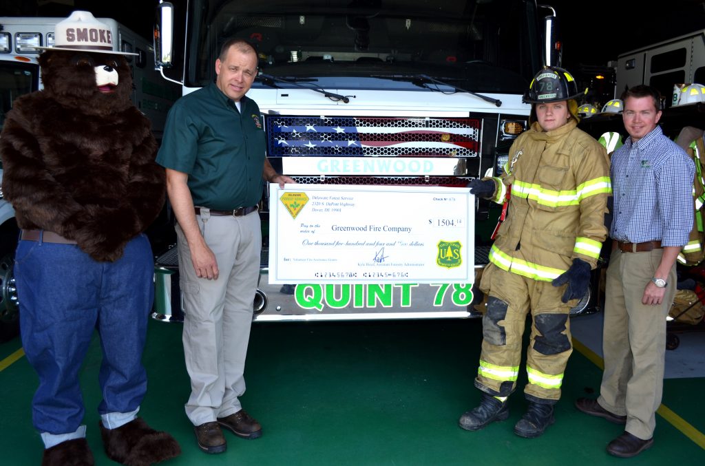 From left, Smokey Bear joined Greenwood Fire Company chief Mark Anderson and firefighter Justin Minton as they received a check for $1504 from the Delaware Forest Service's assistant state forester Kyle Hoyd, who ovesees the agency's wildland fire program. The matching grant will fund equipment used to improve Greenwood's readiness to respond to wildfires. 