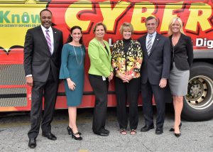 CIO James Collins, DTI; Christine Parker, NSA; Deputy Secretary of Education Karen Field Rogers, DOE; CSO Elayne Starkey, DTI, Governor John Carney; and Kim Paradise, LifeJourney, take a photo in front of a DART bus promoting cyber security.