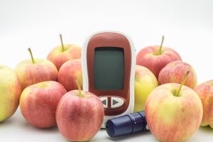 Picture of glucose meter and lancelet surrounded by fresh apples