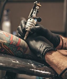 Picture of tattoo artist's arm tattooing an image on a man's forearm