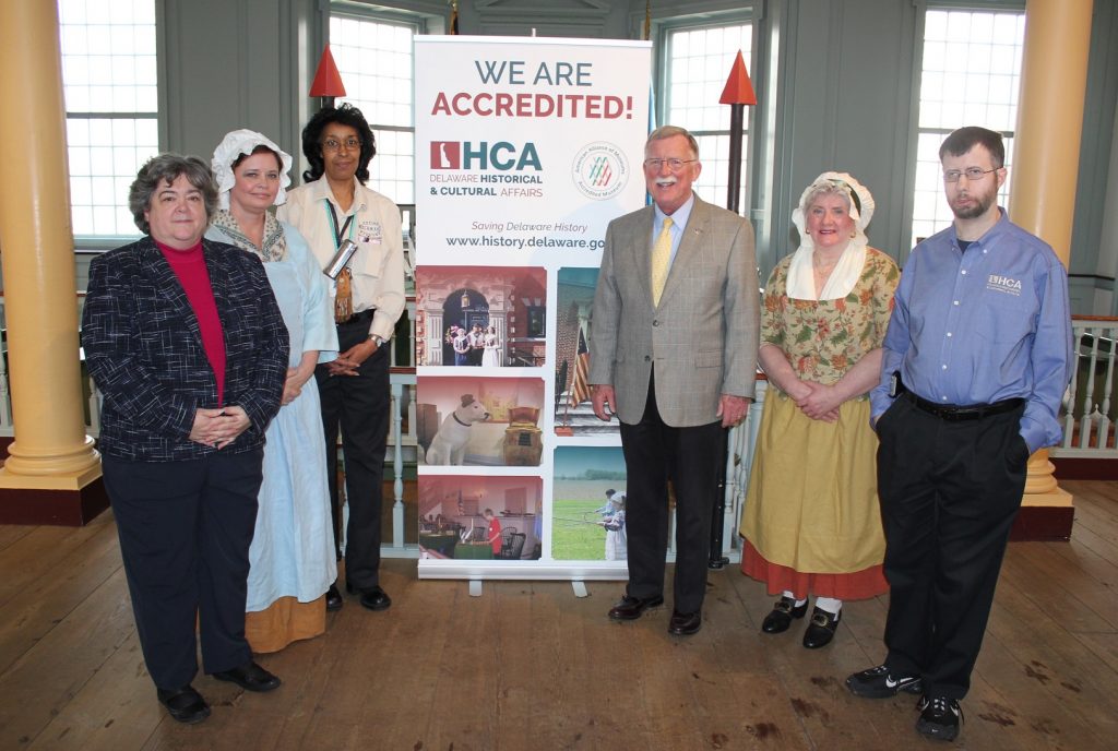 State Sen. Brian Bushweller visits The Old State House in Dover in celebration of the Division of Historical and Cultural Affairs’ accreditation by the American Alliance of Museums. From left: Division Deputy Director Suzanne Savery, historic-site interpreter Valerie Kaufman, site-supervisor Nena Todd, Bushweller, and historic-site interpreters Susan Emory and Gavin Malone