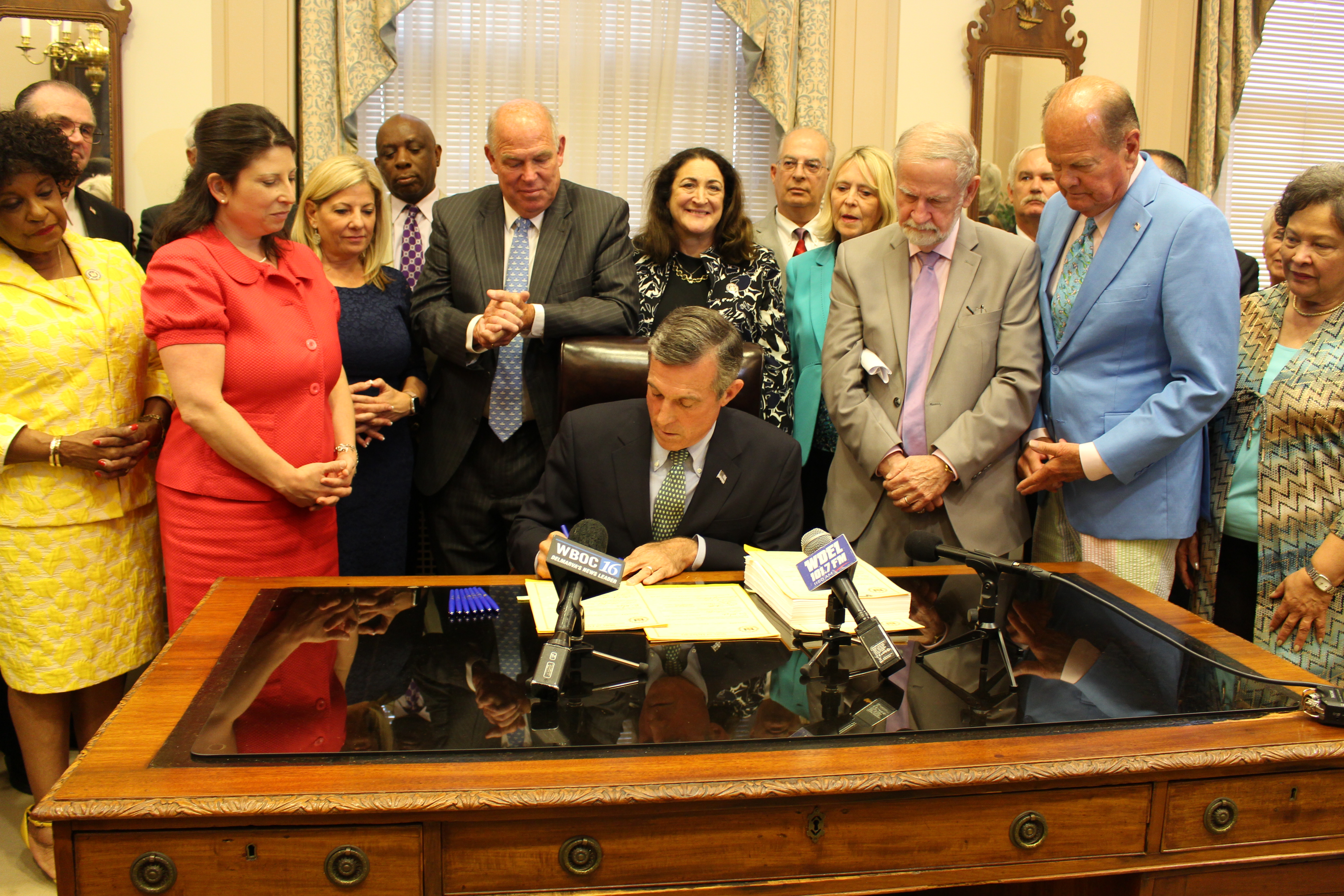 Photo of Governor John Carney signing a bill alongside legislators