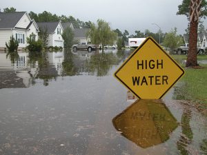 Piture of Neighborhood flooded. Sign warns of high water.