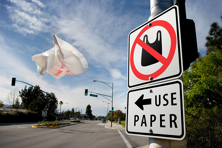 Photo of plastic bag on highway with a sign encouraging using paper bas