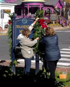 Photo of members of the Sussex Gardeners decorating the Zwaanendael Museum sign for the holidays in 2017.