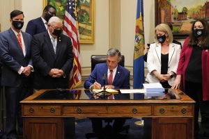 Governor Carney signs Fiscal Year 2022 Operating and Capital Budgets seated at a desk surrounded by members of the General Assembly.