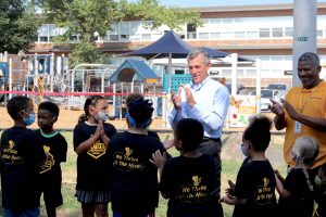 Governor Carney claps his hands with a group of students in front of a park.