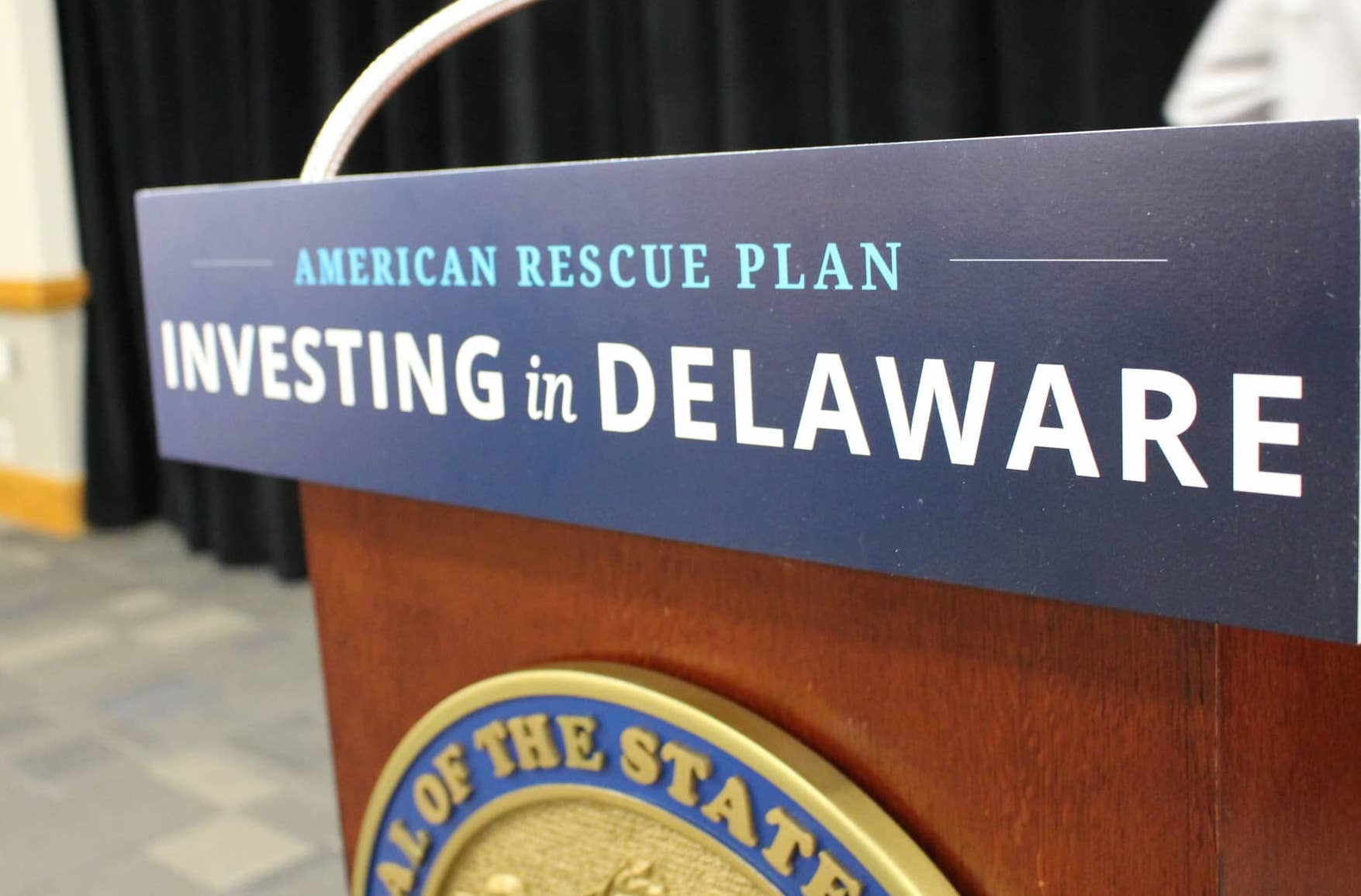 A sign that reads "American Rescue Plan: Investing in Delaware" attached to a podium.