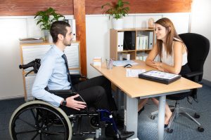 man in wheel chair having a meeting with a woman behind desk.