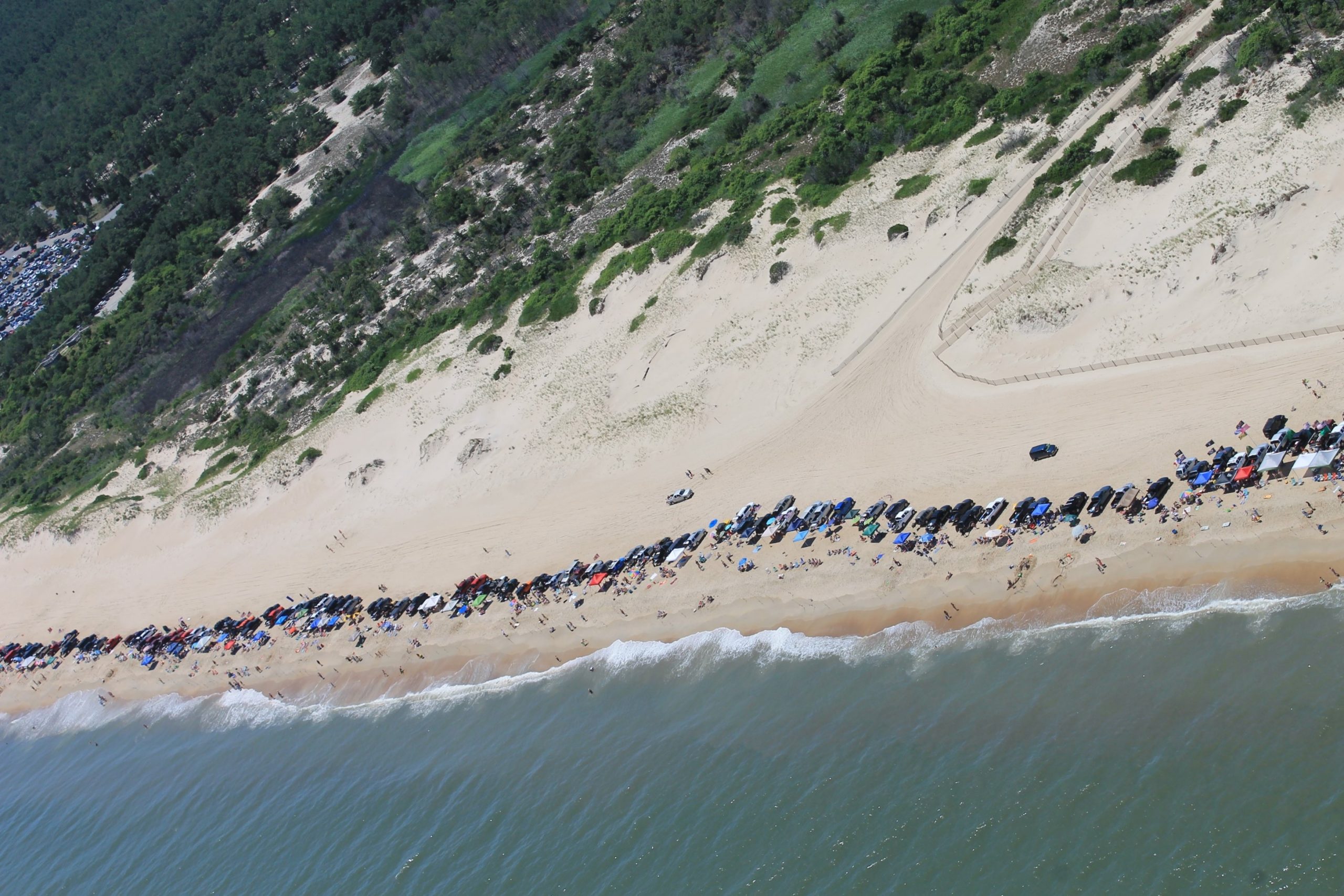 An overhead photo of vehicles along a Delaware beach with coastal water, beach and fauna in the background.