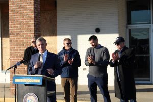 Governor Carney stands behind a podium surrounded by other officials. They are in front of an abandoned store that will be redeveloped.