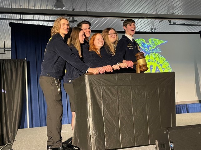 Six FFA students stand at a podium smiling.