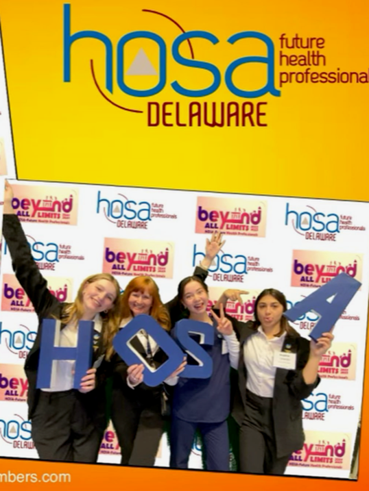 Four Delaware students smile, holding letters that spell HOSA.