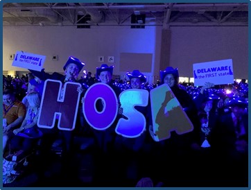 Students stand in front of the camera in the dark, holding letters that spell out HOSA.
