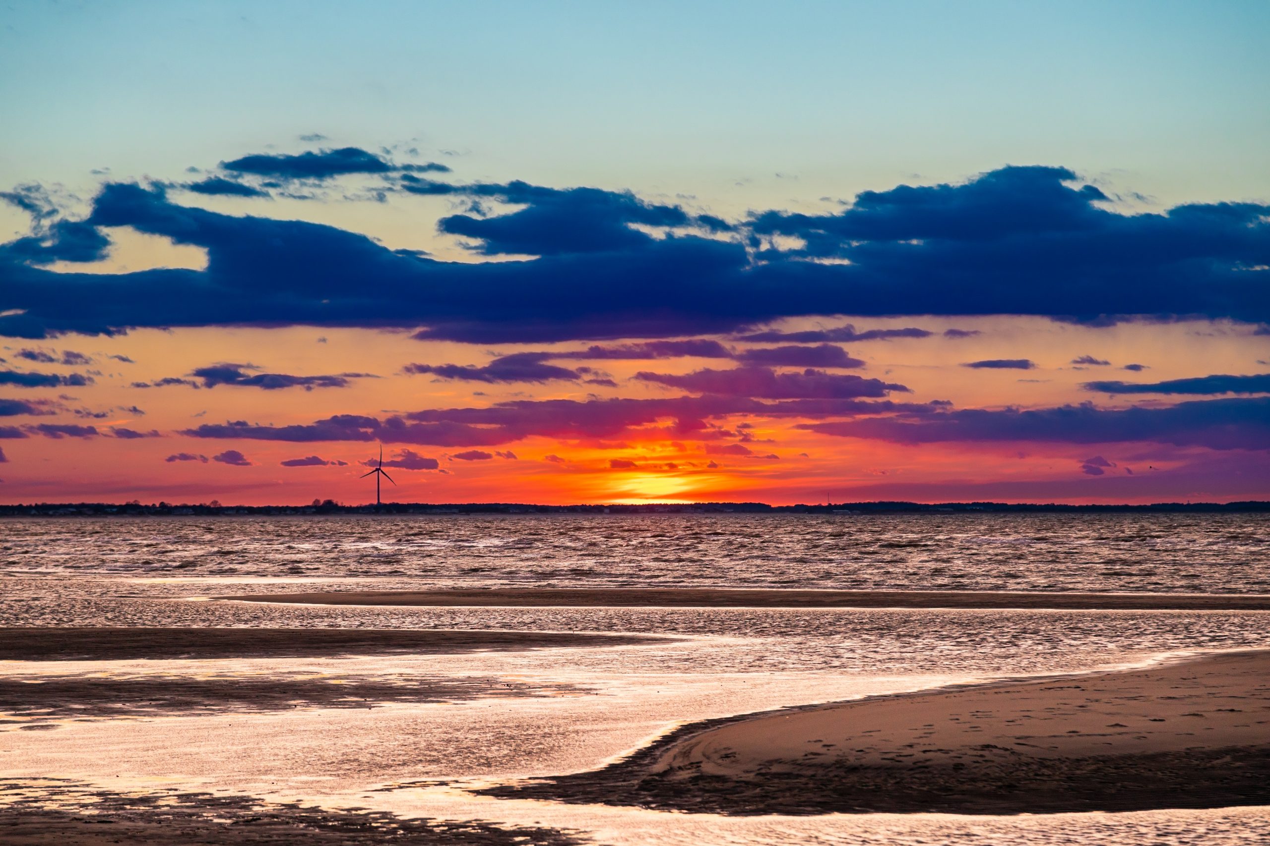 The sun sets across the water along The Point at Cape Henlopen State Park. The sunset is seen from The Point's sandbars.