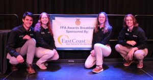 Four FFA students pose next to a FFA sign, smiling at the camera.