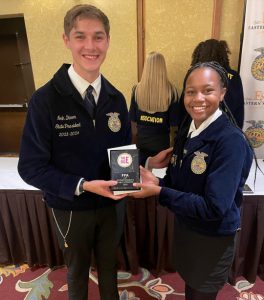 Two FFA students stand, smiling at the camera, and holding a FFA award.
