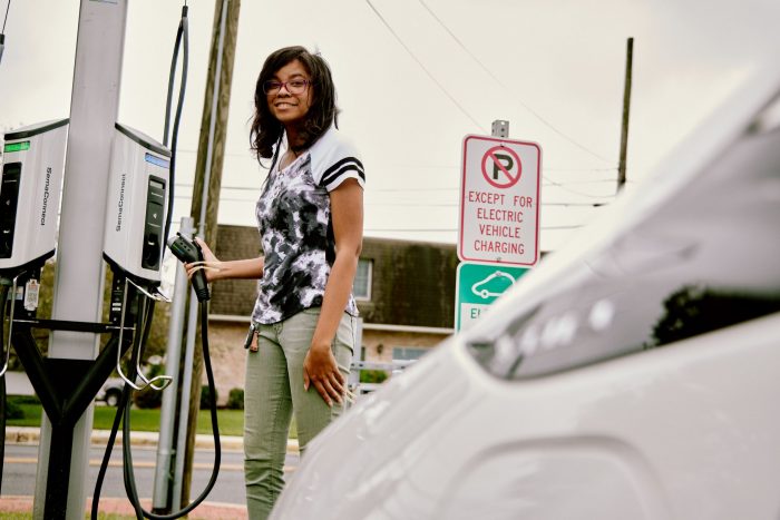 Woman stands holding charging cable at an EV charging station.