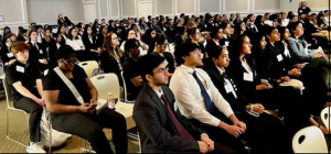 Picture of students dressed in business attire sitting in rows staring at the front of the room.