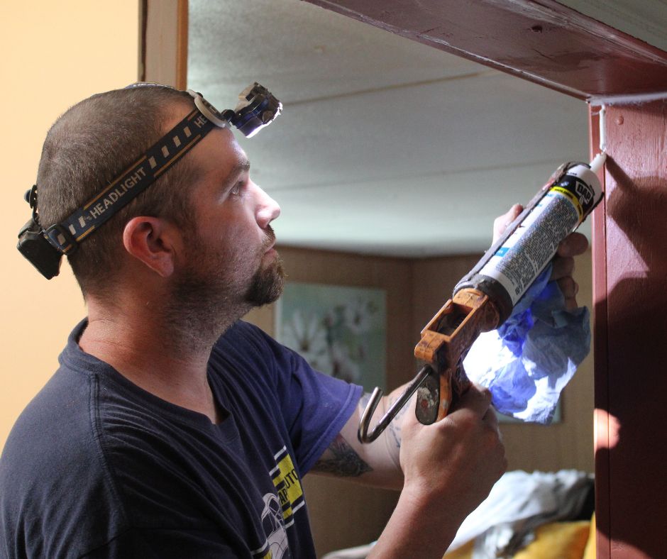 A worker caulks a doorframe to reduce energy waste.