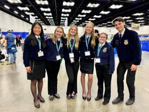 Six students in FFA jackets stand in a row, smiling for the camera.