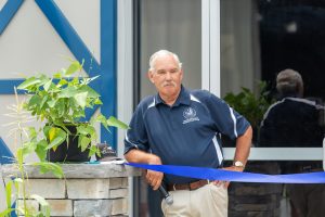 Secretary Scuse stands in front of the Delaware Agriculture Commodities and Education Building with a plant on a stone piling.