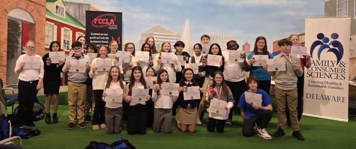 A large group of students stand and sit, smiling for the camera. They are surrounded by FCCLA banners.