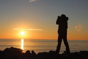 Photographer standing on the rocks to frame a sunset over water