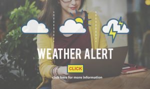 The image depicts a "Weather Alert" notification. It shows a woman working on a laptop with icons representing different weather conditions: a cloud, a cloud with the sun, and a cloud with lightning. Below the text "Weather Alert," there is a clickable button labeled "Click" with the subtext "click here for more information." The overall tone suggests a prompt to check important weather updates.