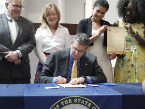 Governor Meyer signs a piece of legislation while legislators and the Lt. Gov. stand behind him.