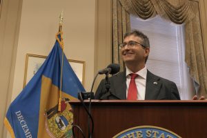Governor Matt Meyer stands at a podium with the Delaware flag in the background.