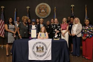Lt. Gov. Kyle Evans Gay signs a Women's Equality Day Proclamation with over a dozen legislators and advocates behind her.