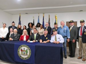 Governor Meyer sits at a table with the state seal with more than a dozen legislators and bill advocates.