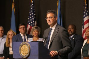 Governor Meyer stands at a podium with legislators standing behind him.