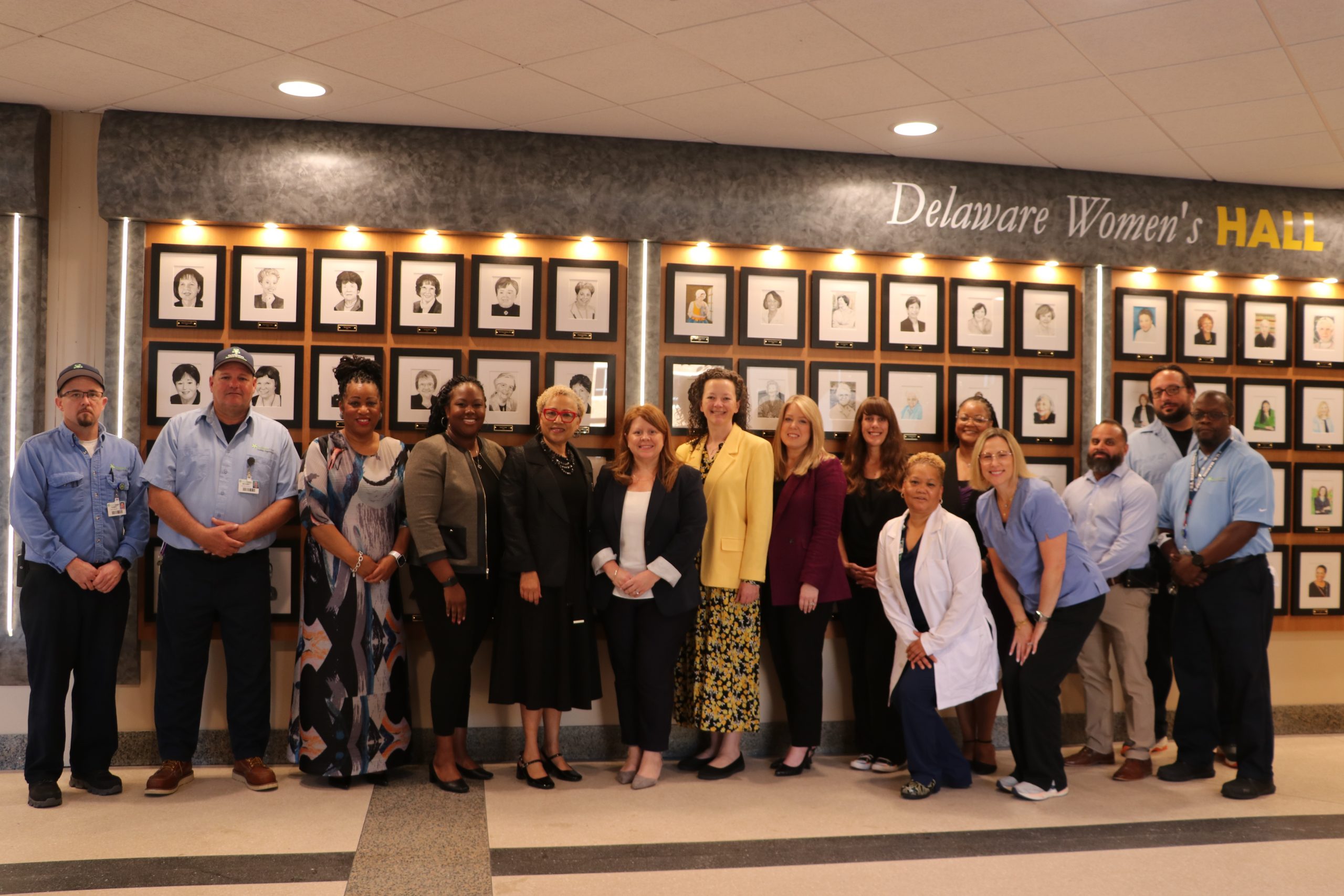 Staff from the Delaware Department of Human Resources, the Office of Women's Advancement and Advocacy, and ChristanaCare stand together in front of the Delaware Women's Hall of Fame Portrait Exhibition at ChristanaCare's Newark Campus, located beside the Center for Heart & Vasular Health lobby.