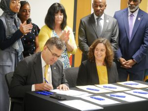 Governor Matt Meyer signs a bill with Secretary of Education Cindy Marten sitting next to him and legislators and advocates behind him.