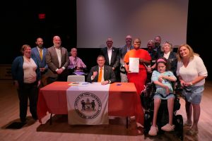 Governor Matt Meyer sits at a table with legislators and advocates signing legislation.