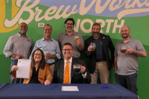 Governor Matt Meyer sits at a table with legislators and advocates as he signs a bill on breweries. Almost everyone is holding a beer.