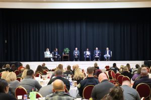Lt. Governor Gay and Commissioner Terra Taylor on stage for a panel with 4 veterans and first responders. the photo is taken with the crowd of conference attendees in the back.