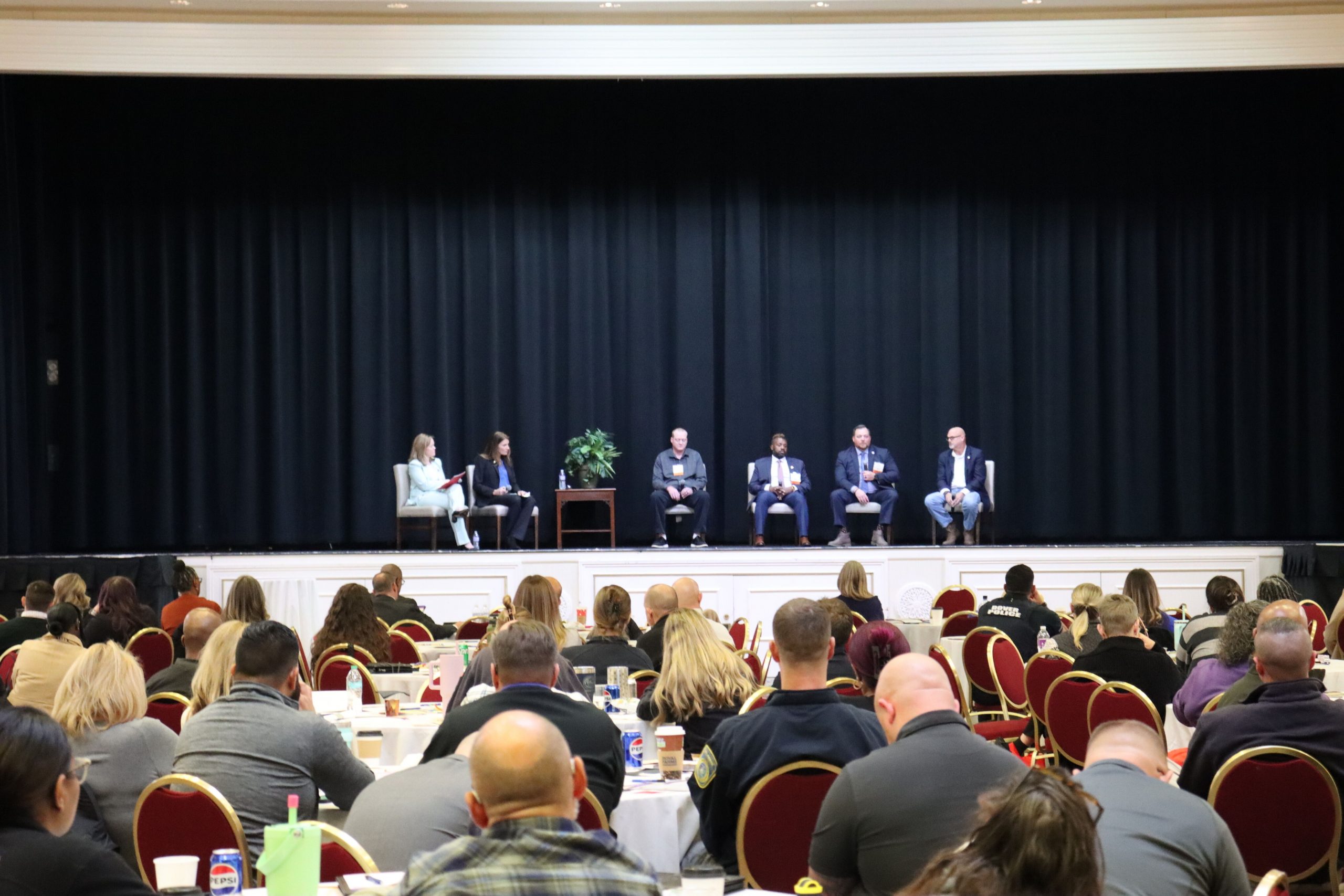 Lt. Governor Gay and Commissioner Terra Taylor on stage for a panel with 4 veterans and first responders. the photo is taken with the crowd of conference attendees in the back.