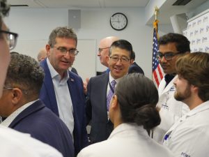 Governor Matt Meyer stands to the left of Beebe President and CEO Dr. David Tam. Both are surrounded by medical students and residents in white coats.