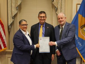 Governor Meyer stands in the middle of Kerri Evelyn Harris on the right and Secretary of Finance Michael Smith on the right, all holding HB255 which was just signed by the Governor.