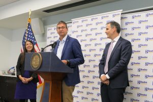 Governor Matt Meyer stands at a podium with a Beebe Healthcare logo background. To his right is DHSS Secretary Christen Linke Young and to his right is Chair of the Delaware Healthcare Commission Dr. Neil Hockstein.