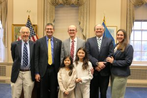 Governor Matt Meyer and recently sworn in Family Court Commissioner Mark Hudson face forward smiling for a photo, surrounded by friends and family of Hudson.