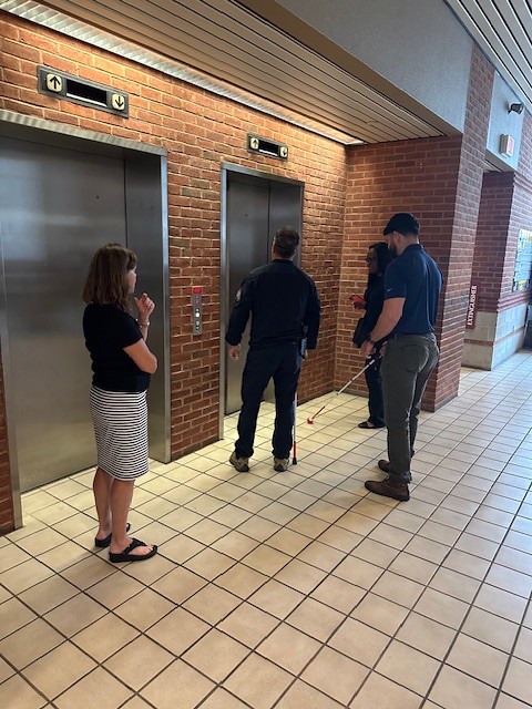 A woman guides two male police officers through sensitivity training for visual impairments.