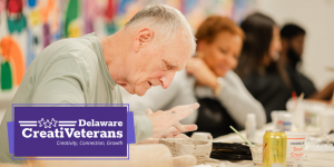 A man concentrates while shaping clay at a workshop table, with other participants blurred in the background. A purple graphic in the lower left reads “Delaware CreatiVeterans” with the tagline “Creativity, Connection, Growth.”