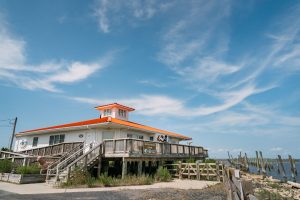 visitors enjoy the view from the DuPont Nature Center deck overlooking the beach. the building behind them with a beautiful clear sky as the backdrop.