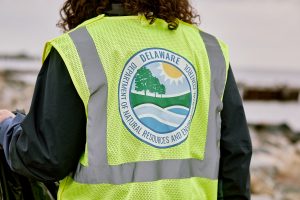 Photo zoomed in of the just the back of a man wearing a neon safety vest with the DNREC logo on the back.