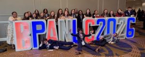Students pose standing in front of large letters that spell BPANLC2026. Three students sit in front of the letters wearing suits.